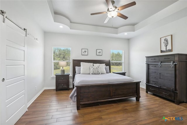 bedroom with a raised ceiling, ceiling fan, and a barn door