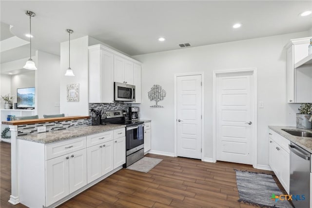 kitchen with appliances with stainless steel finishes, hanging light fixtures, kitchen peninsula, decorative backsplash, and white cabinets