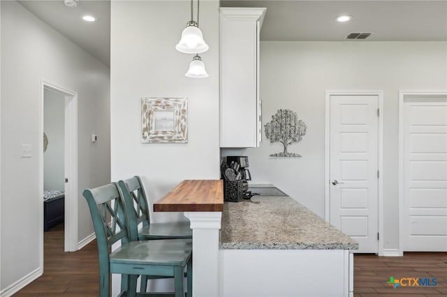 kitchen with decorative light fixtures, white cabinetry, kitchen peninsula, a breakfast bar area, and dark wood-type flooring