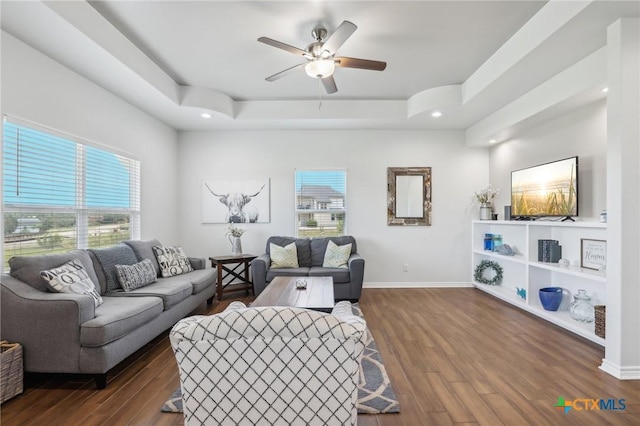 living room with ceiling fan, dark hardwood / wood-style flooring, a wealth of natural light, and a tray ceiling