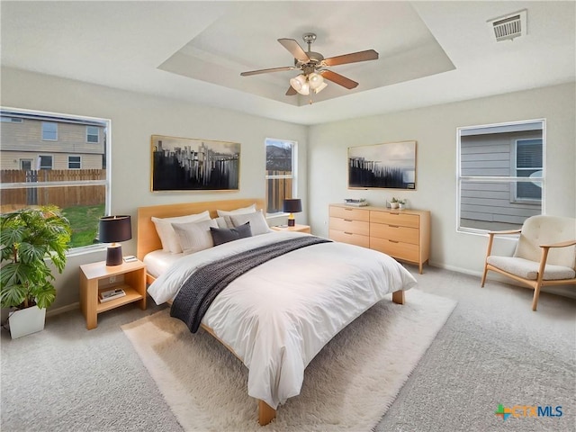 bedroom featuring baseboards, visible vents, a tray ceiling, and light colored carpet