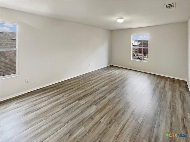 empty room with wood finished floors, visible vents, and baseboards