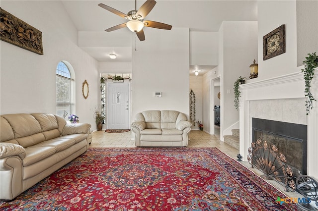 living room with a towering ceiling, ceiling fan, and a tile fireplace