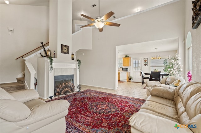 tiled living room with a tiled fireplace, high vaulted ceiling, ceiling fan with notable chandelier, and crown molding