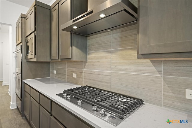 kitchen with tasteful backsplash, dark brown cabinetry, stainless steel appliances, wall chimney range hood, and light hardwood / wood-style floors