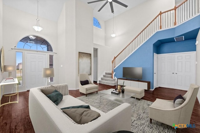 living room featuring visible vents, stairway, a high ceiling, ceiling fan, and wood finished floors