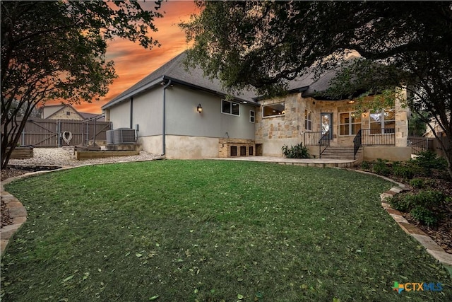 back house at dusk featuring a yard and central AC