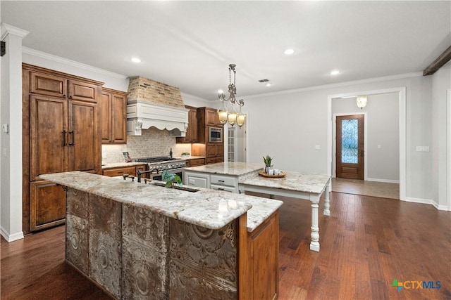 kitchen with a center island with sink, light stone countertops, decorative backsplash, sink, and decorative light fixtures