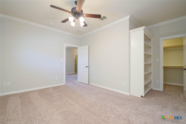 unfurnished bedroom featuring ceiling fan, a closet, a walk in closet, crown molding, and light colored carpet