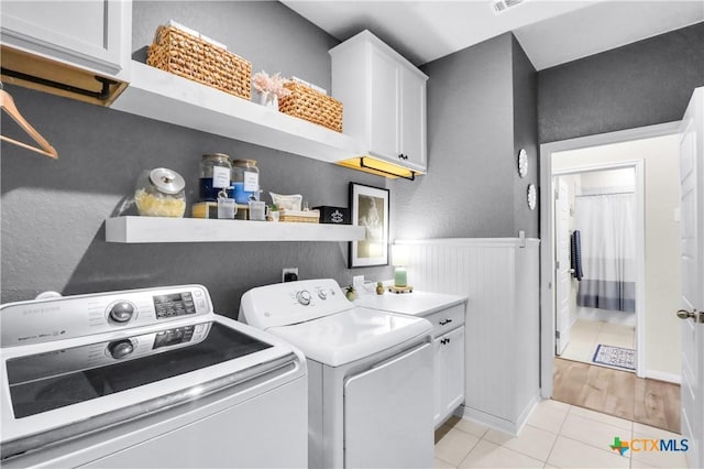 washroom featuring wainscoting, washer and dryer, cabinet space, and light tile patterned flooring