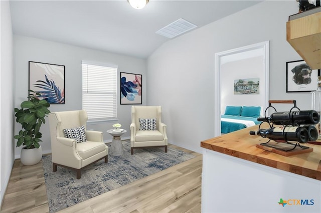 living area featuring visible vents, vaulted ceiling, and light wood finished floors