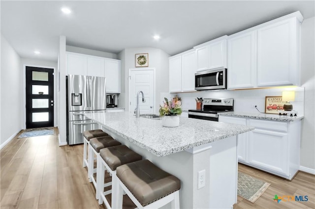 kitchen with a sink, light stone countertops, light wood-type flooring, appliances with stainless steel finishes, and a kitchen island with sink