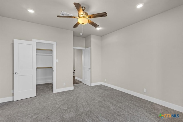 unfurnished bedroom with a closet, a walk in closet, ceiling fan, and dark carpet