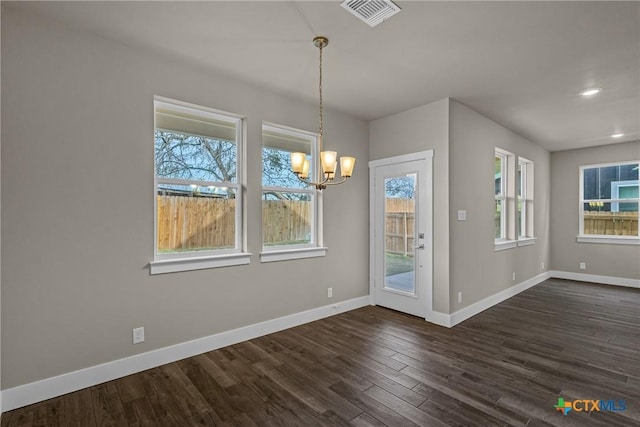 unfurnished dining area with an inviting chandelier, plenty of natural light, and dark wood-type flooring