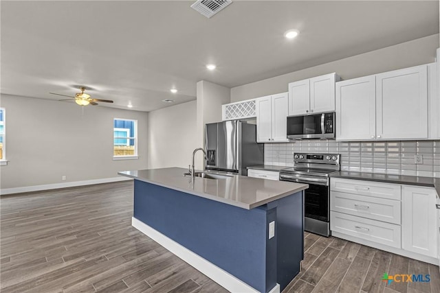 kitchen featuring appliances with stainless steel finishes, an island with sink, dark hardwood / wood-style floors, white cabinets, and backsplash