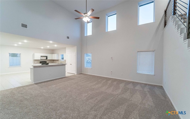 unfurnished living room featuring a towering ceiling, light carpet, and ceiling fan