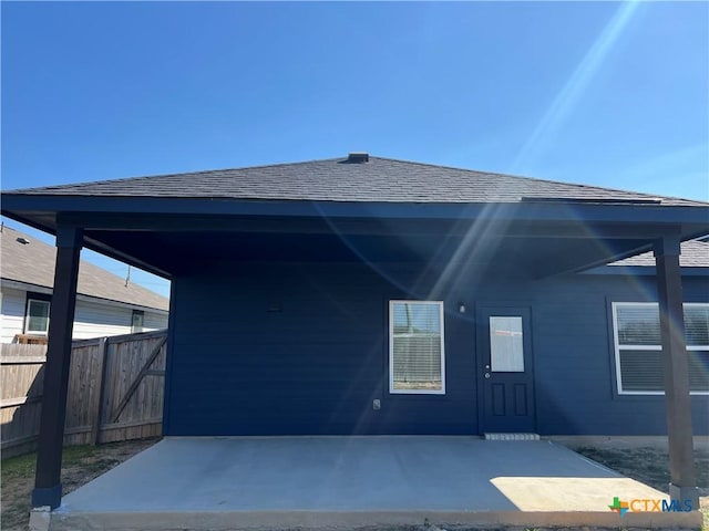 exterior space with a carport, a patio area, roof with shingles, and fence