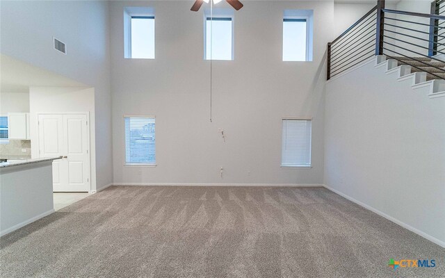 unfurnished living room featuring a ceiling fan, light colored carpet, visible vents, and baseboards