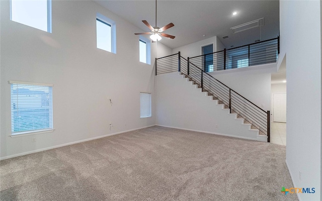 unfurnished living room with light colored carpet, ceiling fan, and a high ceiling