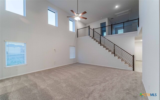 unfurnished living room featuring a wealth of natural light, a ceiling fan, stairway, and carpet flooring