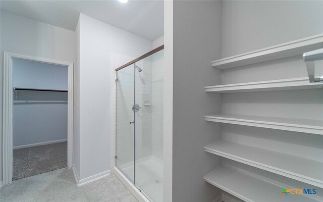 full bathroom featuring a stall shower, a spacious closet, and baseboards