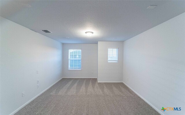 unfurnished room featuring baseboards, visible vents, a textured ceiling, and light colored carpet