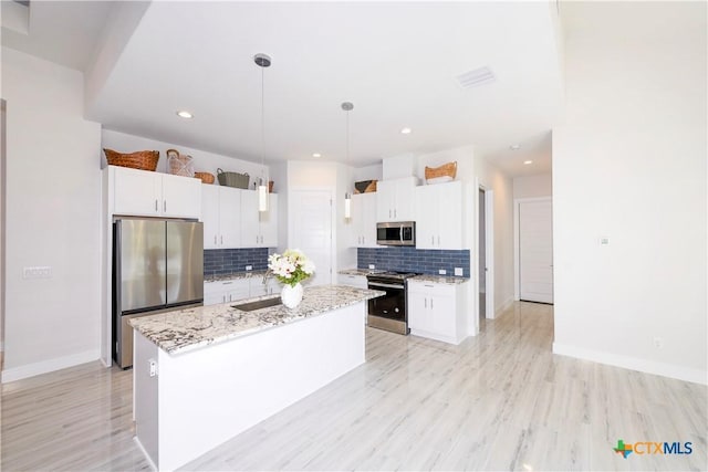 kitchen with light stone countertops, hanging light fixtures, tasteful backsplash, a center island with sink, and appliances with stainless steel finishes