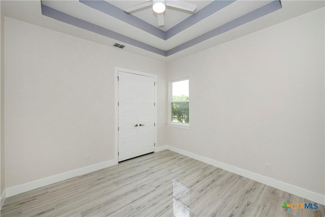 empty room featuring light wood-type flooring, a tray ceiling, and ceiling fan