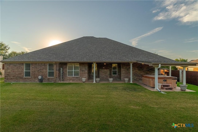 ranch-style home with a hot tub, roof with shingles, a front lawn, and brick siding