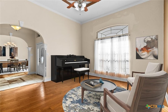 sitting room with arched walkways, crown molding, wood finished floors, baseboards, and ceiling fan with notable chandelier