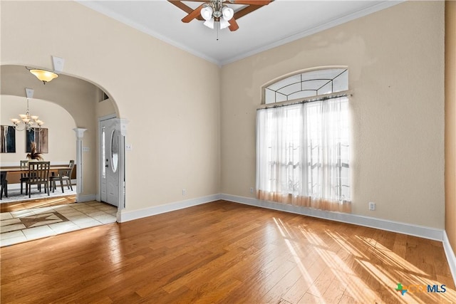 empty room with ornamental molding, arched walkways, baseboards, and wood finished floors