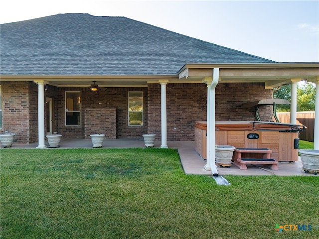 back of property with a shingled roof, brick siding, a yard, and a hot tub