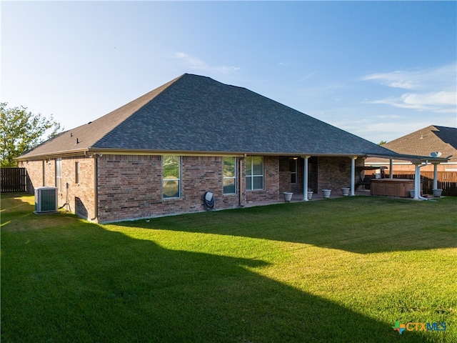 back of house with brick siding, fence, roof with shingles, a lawn, and a hot tub