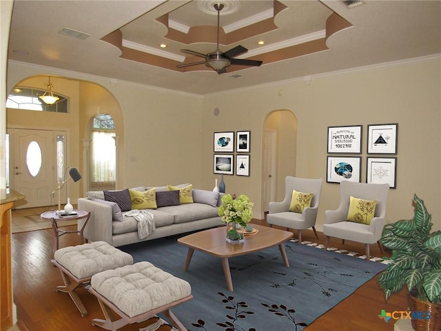 living room featuring arched walkways, a tray ceiling, wood finished floors, and visible vents