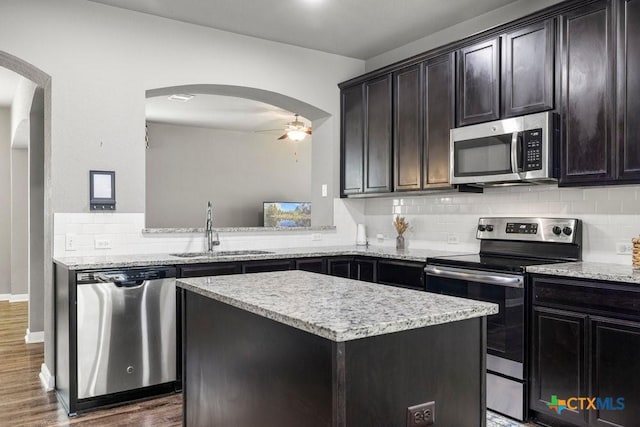 kitchen with sink, dark wood-type flooring, backsplash, a kitchen island, and appliances with stainless steel finishes