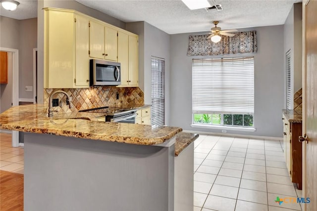 106 Hamlet Ct, Victoria, TX 77901 - kitchen with stainless steel appliances, cream cabinets, a peninsula, a ceiling fan, and backsplash