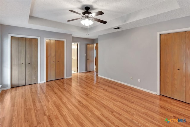 106 Hamlet Ct, Victoria, TX 77901 - unfurnished bedroom featuring multiple closets, a tray ceiling, light wood-style floors, a textured ceiling, and a ceiling fan