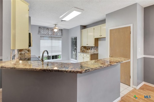 106 Hamlet Ct, Victoria, TX 77901 - kitchen featuring a peninsula, backsplash, light stone counters, and a textured ceiling