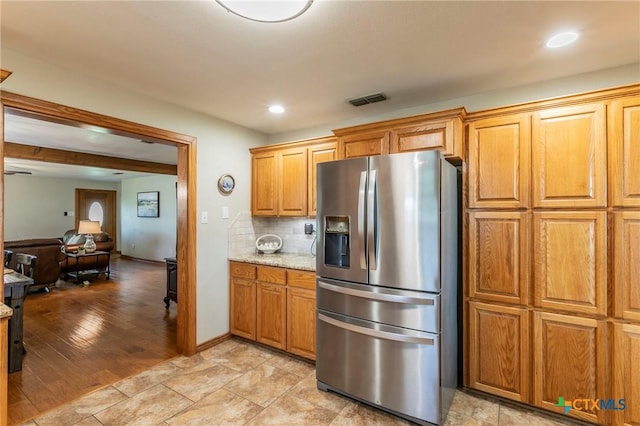 kitchen featuring stainless steel fridge, tasteful backsplash, brown cabinetry, and visible vents