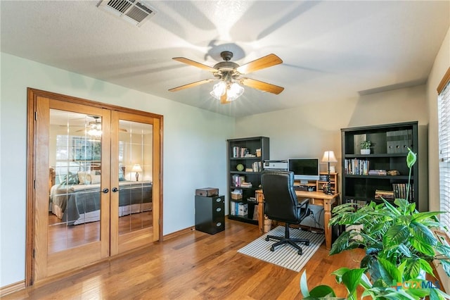 office space featuring french doors, a ceiling fan, wood finished floors, and visible vents
