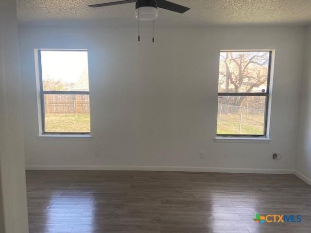 empty room with a textured ceiling, ceiling fan, plenty of natural light, and dark wood-type flooring