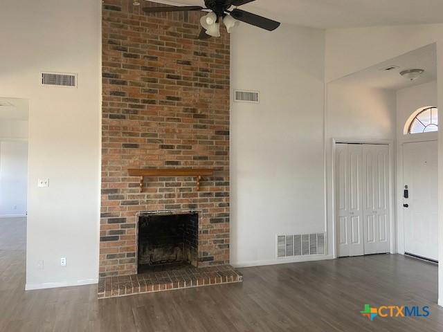 unfurnished living room with ceiling fan, dark wood-type flooring, high vaulted ceiling, and a fireplace