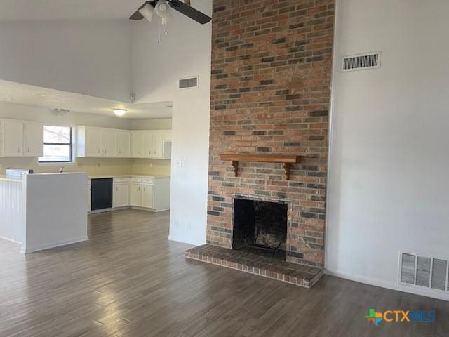 unfurnished living room featuring a towering ceiling, a fireplace, ceiling fan, and dark hardwood / wood-style floors