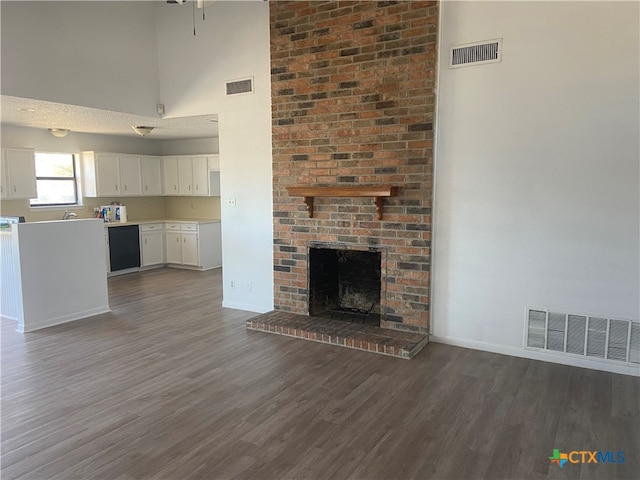 unfurnished living room with a towering ceiling, dark hardwood / wood-style flooring, and a brick fireplace