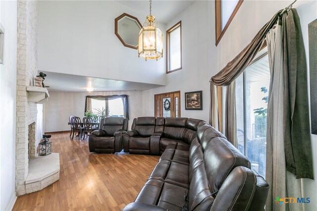 living room with a chandelier, hardwood / wood-style flooring, a brick fireplace, and a towering ceiling