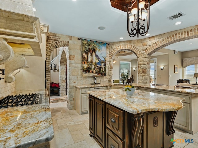 kitchen featuring gas cooktop, a center island, light stone counters, dark brown cabinetry, and decorative light fixtures