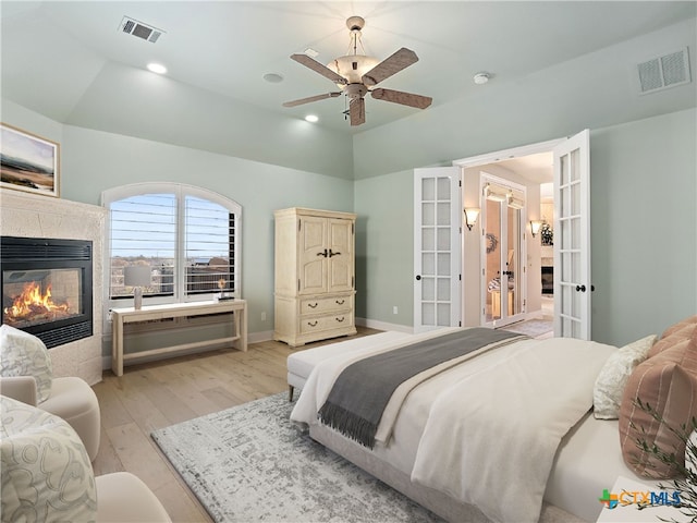 bedroom with vaulted ceiling, a tiled fireplace, ceiling fan, light hardwood / wood-style floors, and french doors