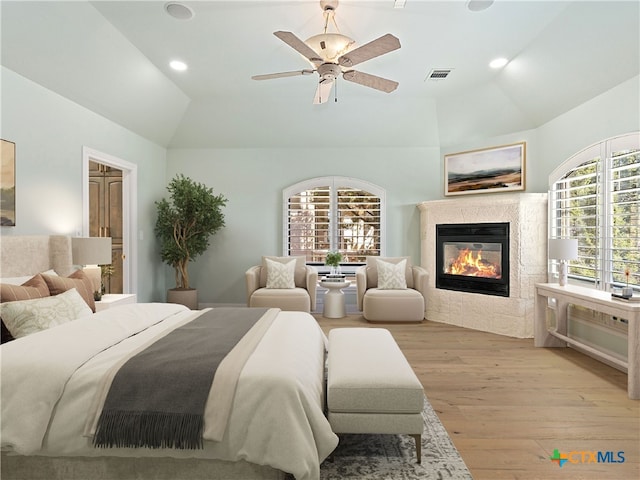 bedroom featuring a tiled fireplace, vaulted ceiling, ceiling fan, and light wood-type flooring