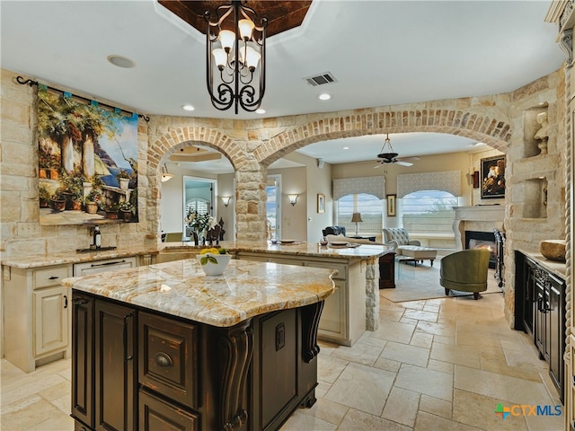 kitchen with decorative light fixtures, a center island, dark brown cabinetry, ceiling fan, and light stone counters