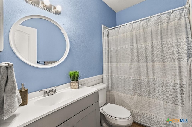 bathroom with vanity, toilet, and a wainscoted wall